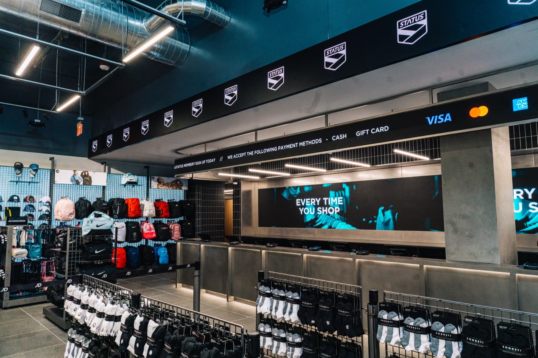 Inside a JD Sports store: the accessory wall and checkout counter under the STATUS fascia